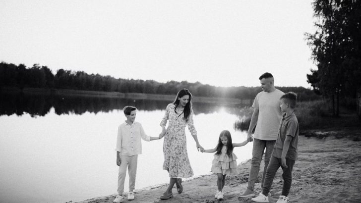 Monochrome photo of a family walking hand in hand along a serene lakeshore.